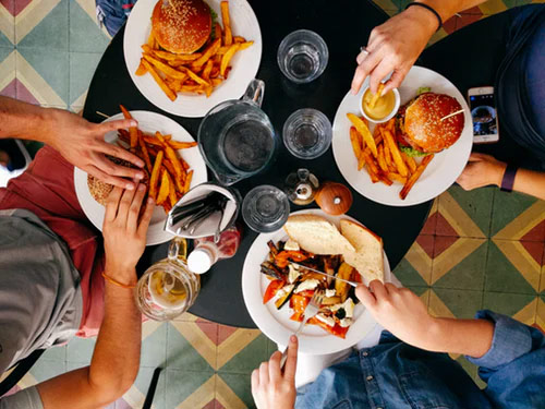 Overhead view of four young people enjoying a dinner of hamburgers and fries